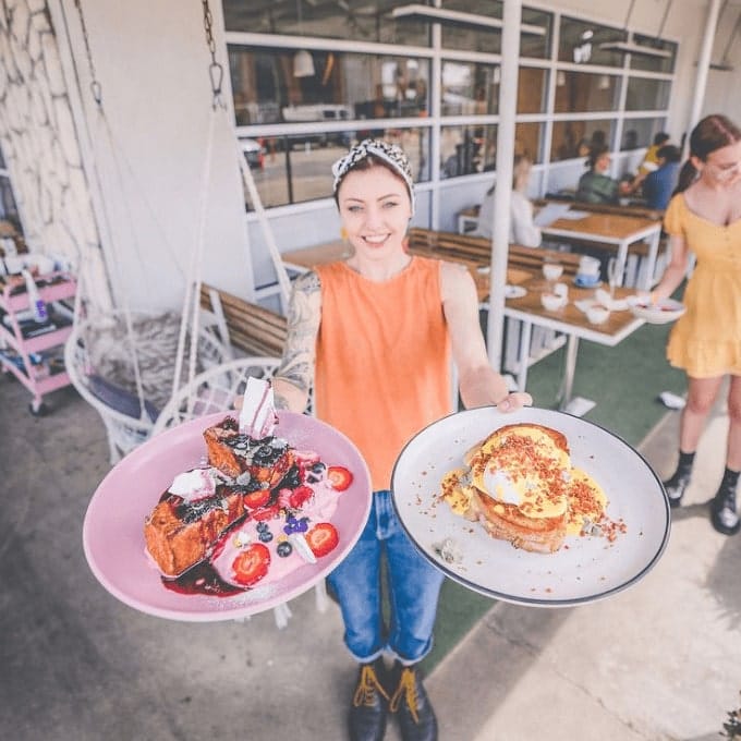 Woman standing outside a cafe that's dog friendly around Geelong and Surrounds holding plates of food