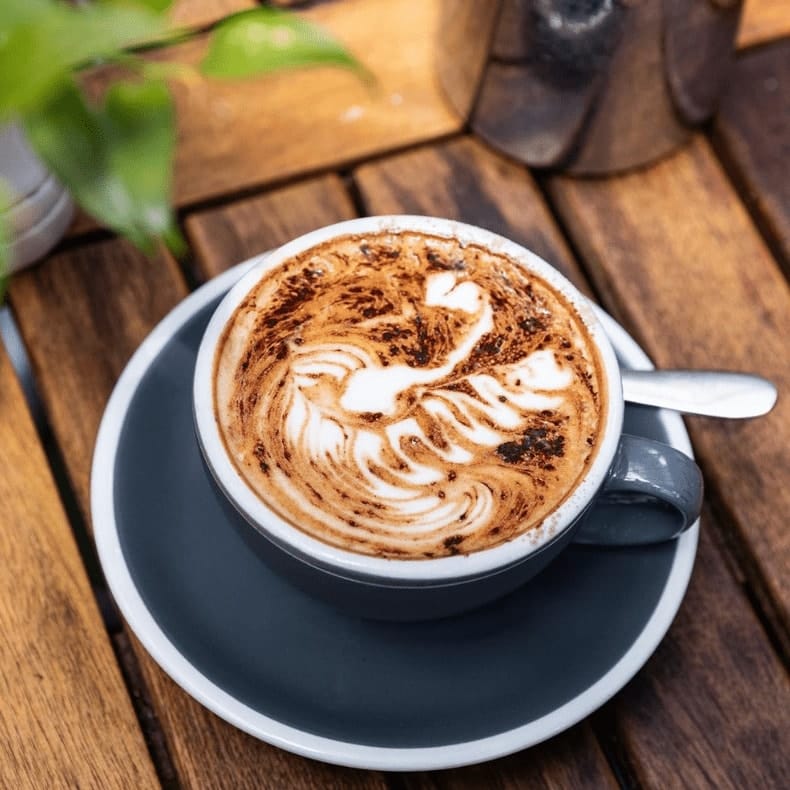 Ceramic coffee cup sits on a wooden table, with a small amount of steam rising at a dog friendly cafe