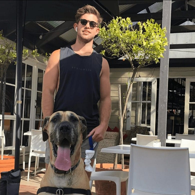 A man standing outside a pet friendly cafe in Melbourne with his dog on a leash in front of him