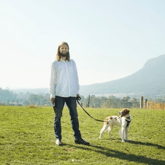 A man standing in the grassy area of this pet friendly cafe outside Eastern Melbourne as he holds his dog by the leash to the side