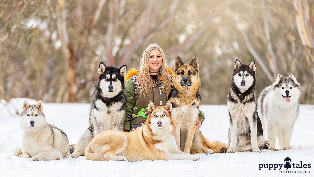 a woman posing for the camera with her six dogs